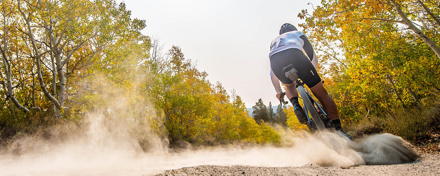 Gravel Cyclist riding fast with Fall colored treeline 