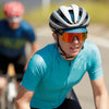 female road cyclist wearing emerald motion jersey being followed by another cyclist